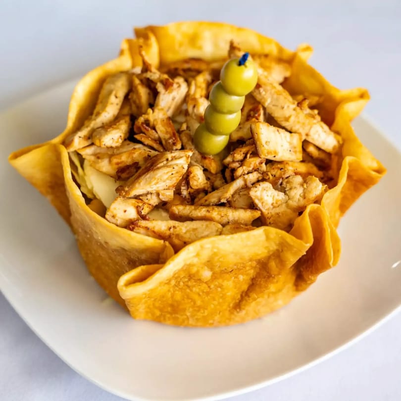 Chicken salad in a crispy tortilla bowl, garnished with green olives on a skewer.
