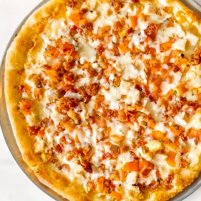 A close-up, overhead view of a Tuscan Bistro pizza with white sauce, chicken, and orange toppings.